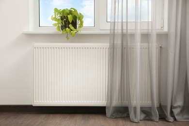 Photo of Beautiful houseplant on window sill and modern radiator at home. Central heating system