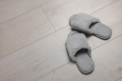 Photo of Pair of soft grey slippers on wooden floor, above view. Space for text