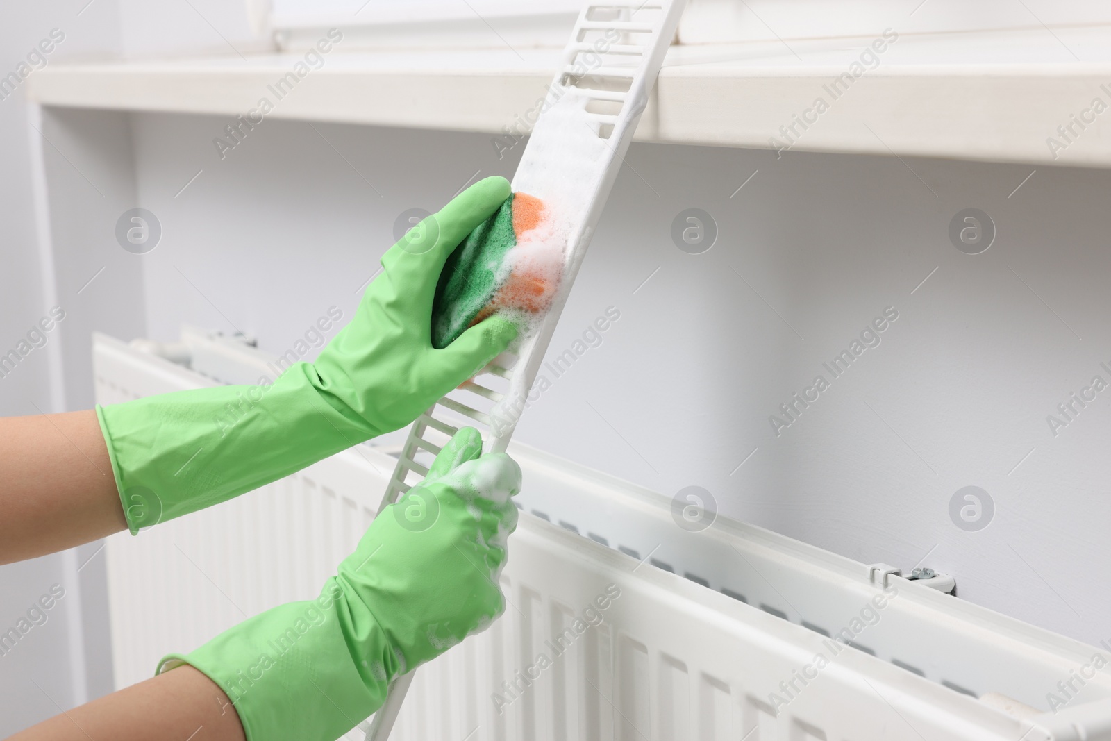 Photo of Woman washing radiator grill with sponge and detergent indoors, closeup