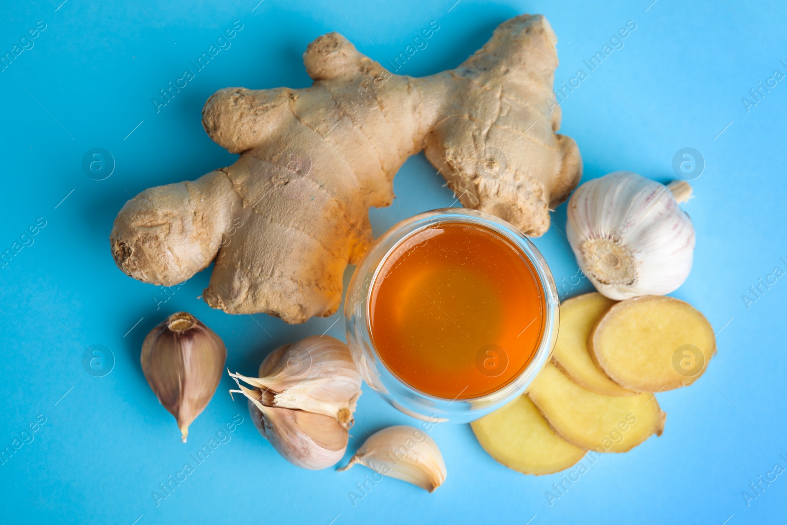 Photo of Fresh garlic and other natural cold remedies on light blue background, flat lay