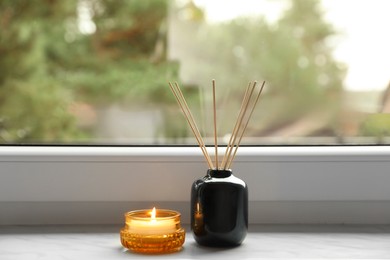 Aromatic reed air freshener and scented candle on windowsill indoors