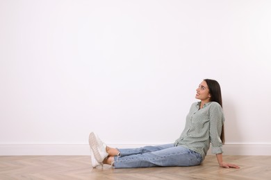 Photo of Young woman sitting on floor near white wall indoors. Space for text