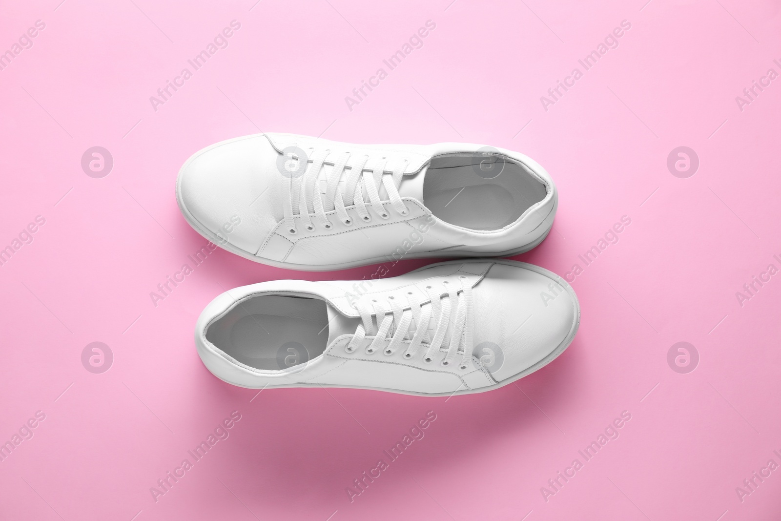 Photo of Pair of stylish white sneakers on pink background, top view