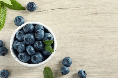 Photo of Bowl of fresh tasty blueberries with leaves on white wooden table, flat lay. Space for text