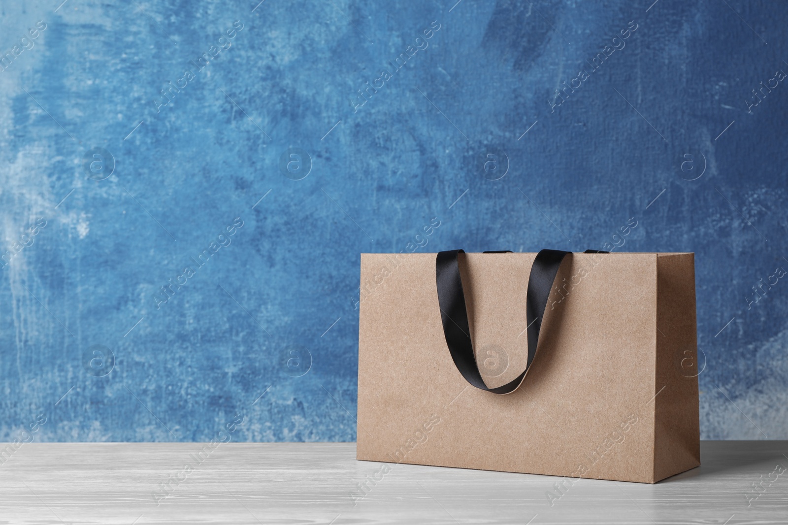 Photo of Paper shopping bag with handles on table against color wall. Mock up for design