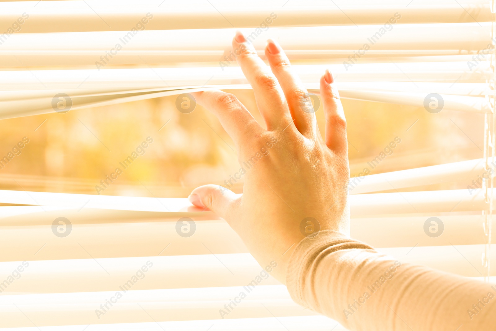 Photo of Woman separating slats of white blinds indoors, closeup