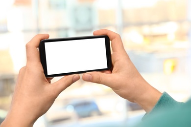 Photo of Man holding smartphone with blank screen on blurred background, closeup of hands. Space for text