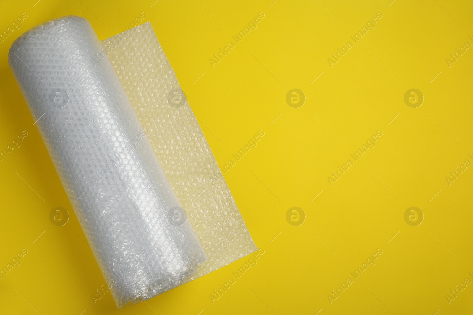 Photo of Bubble wrap roll on yellow background, top view. Space for text