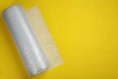 Photo of Bubble wrap roll on yellow background, top view. Space for text