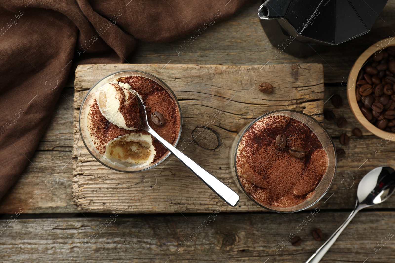 Photo of Delicious tiramisu in glasses, spoons and coffee beans on wooden table, top view