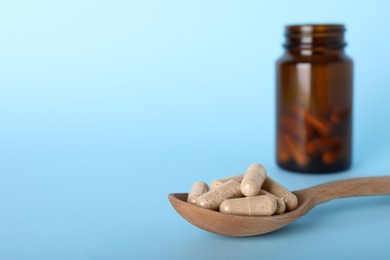Photo of Spoon with gelatin capsules and bottle on light blue background, space for text