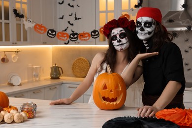 Photo of Couple in scary bride and pirate costumes with carved pumpkin indoors, space for text. Halloween celebration