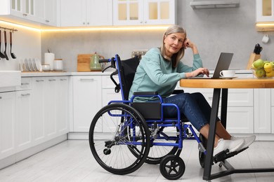 Woman in wheelchair using laptop at table in home office