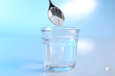 Photo of Adding baking soda into glass of water on light blue background