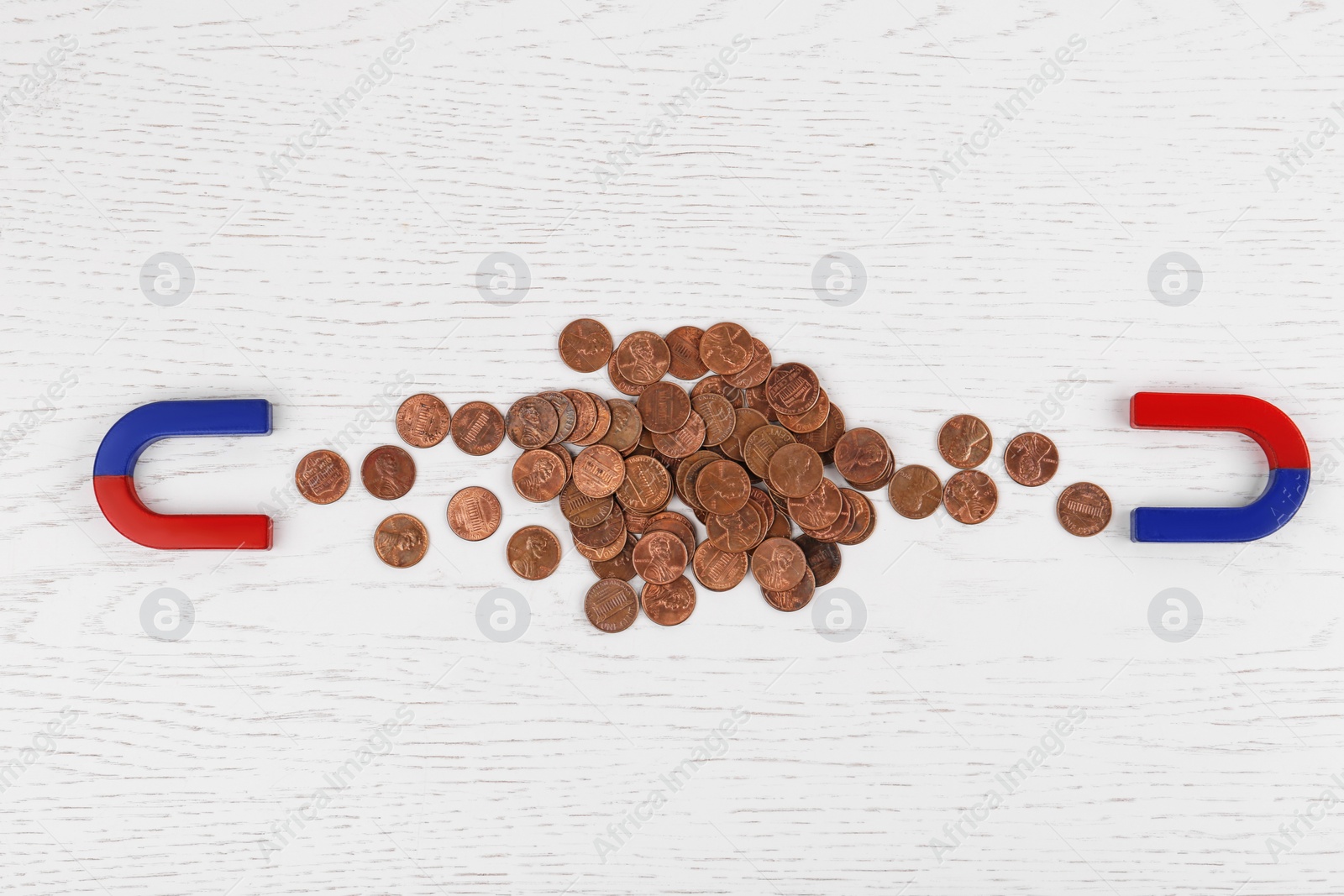 Photo of Magnets attracting coins on white wooden table, flat lay