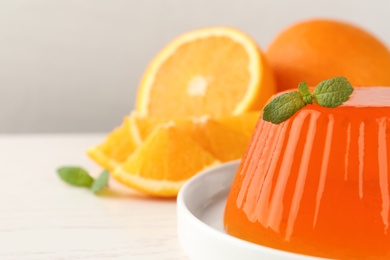 Plate of tasty orange jelly with mint on white table, closeup. Space for text