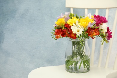 Photo of Beautiful spring freesia flowers in vase on chair. Space for text