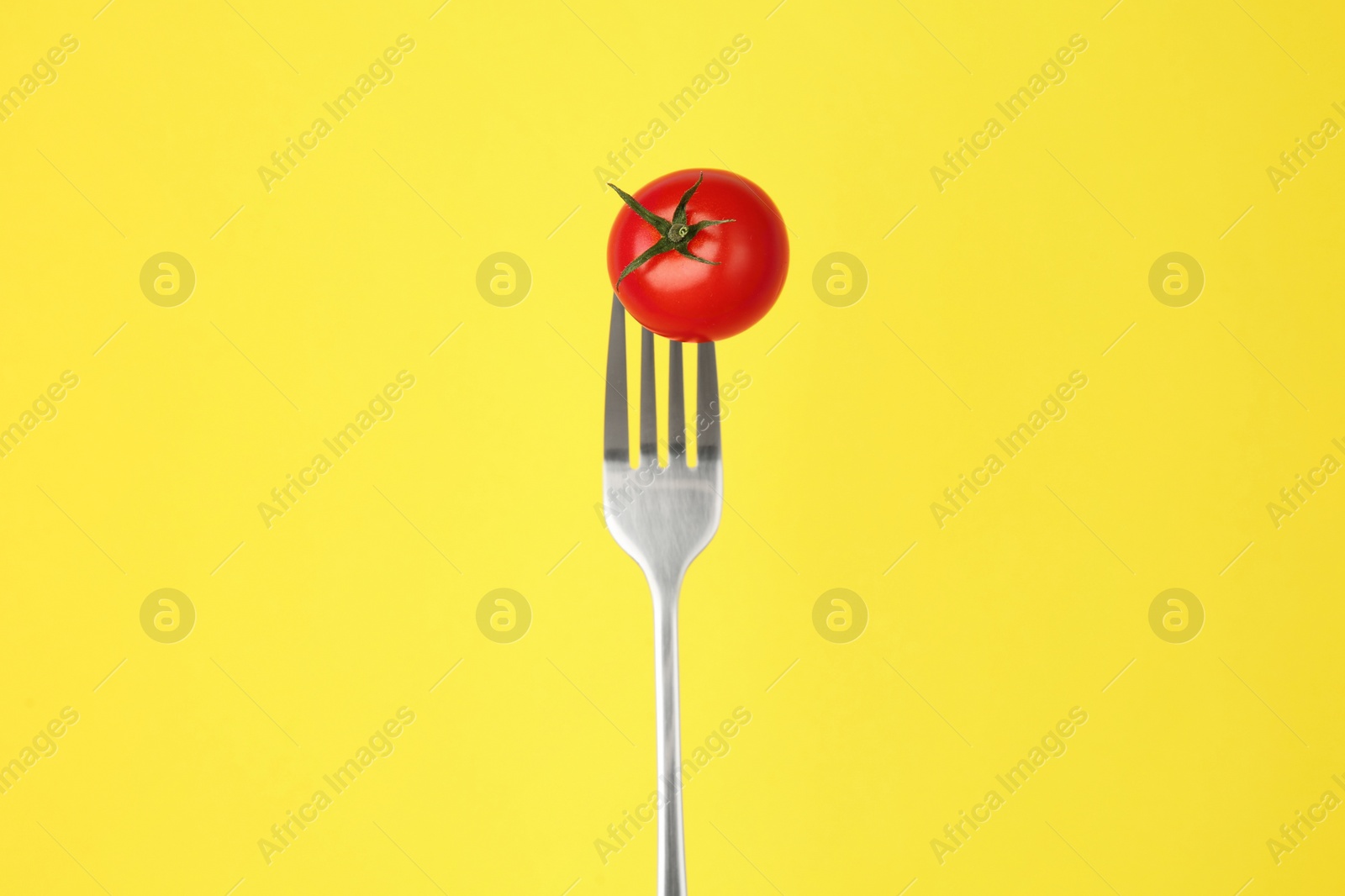 Photo of Fork with cherry tomato on yellow background
