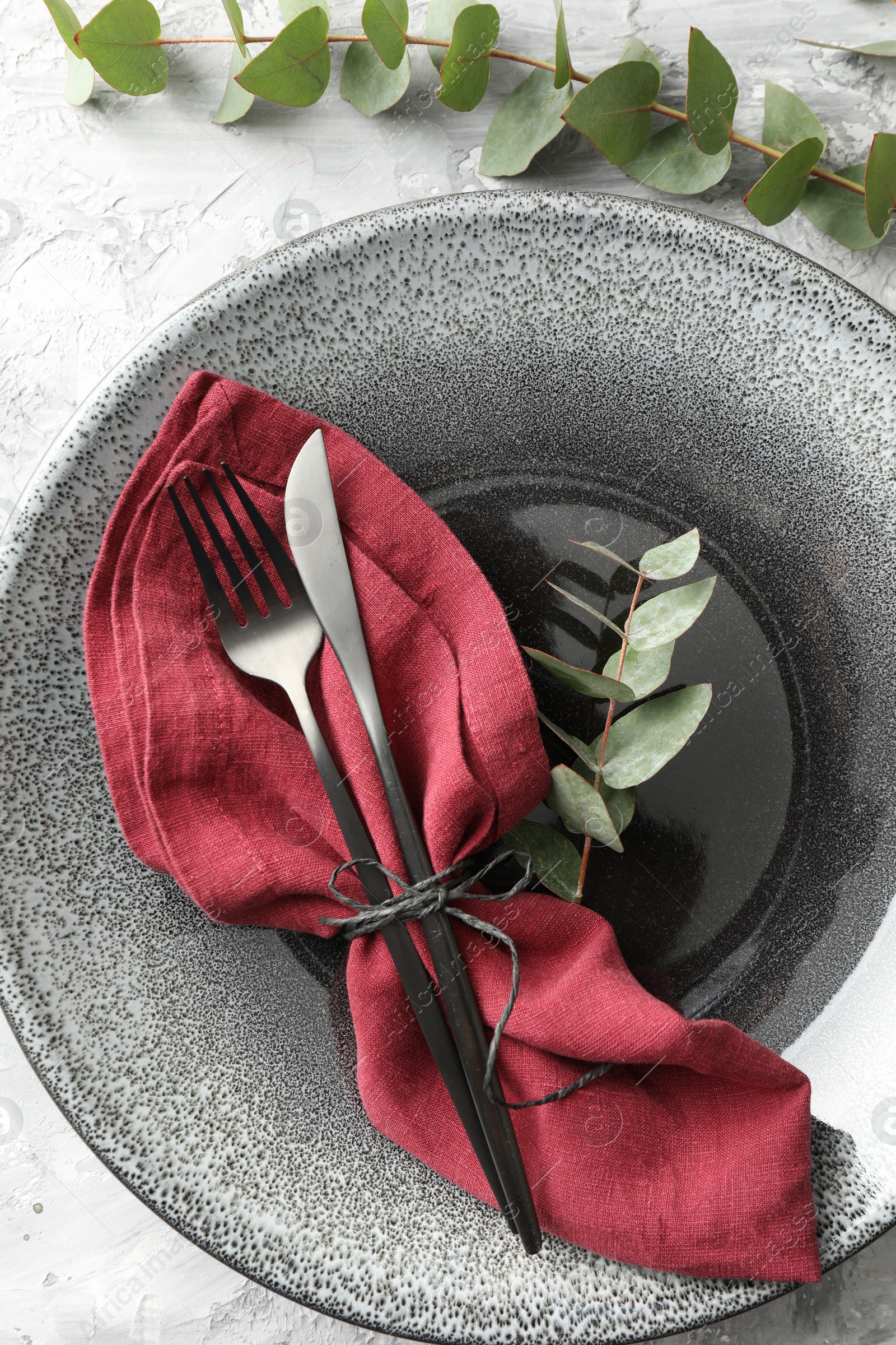 Photo of Stylish setting with cutlery, napkin, eucalyptus branches and plate on grey textured table, top view