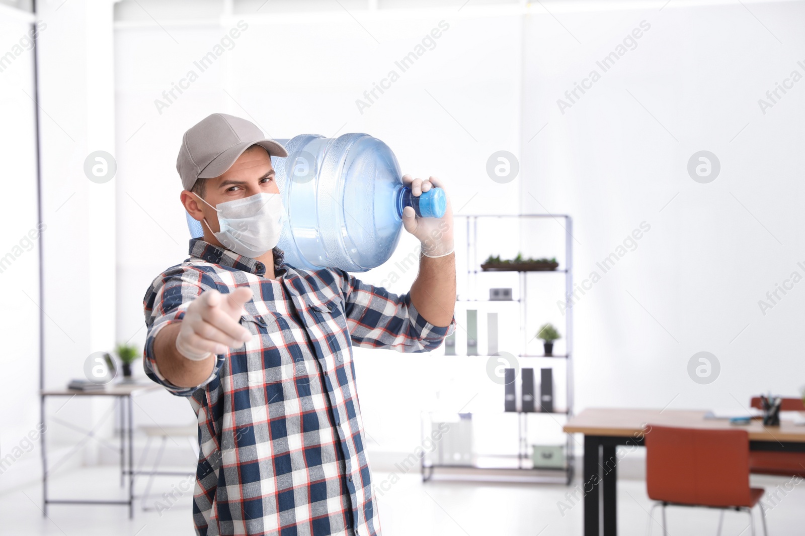 Photo of Courier in mask with bottle of cooler water indoors. Delivery during coronavirus quarantine