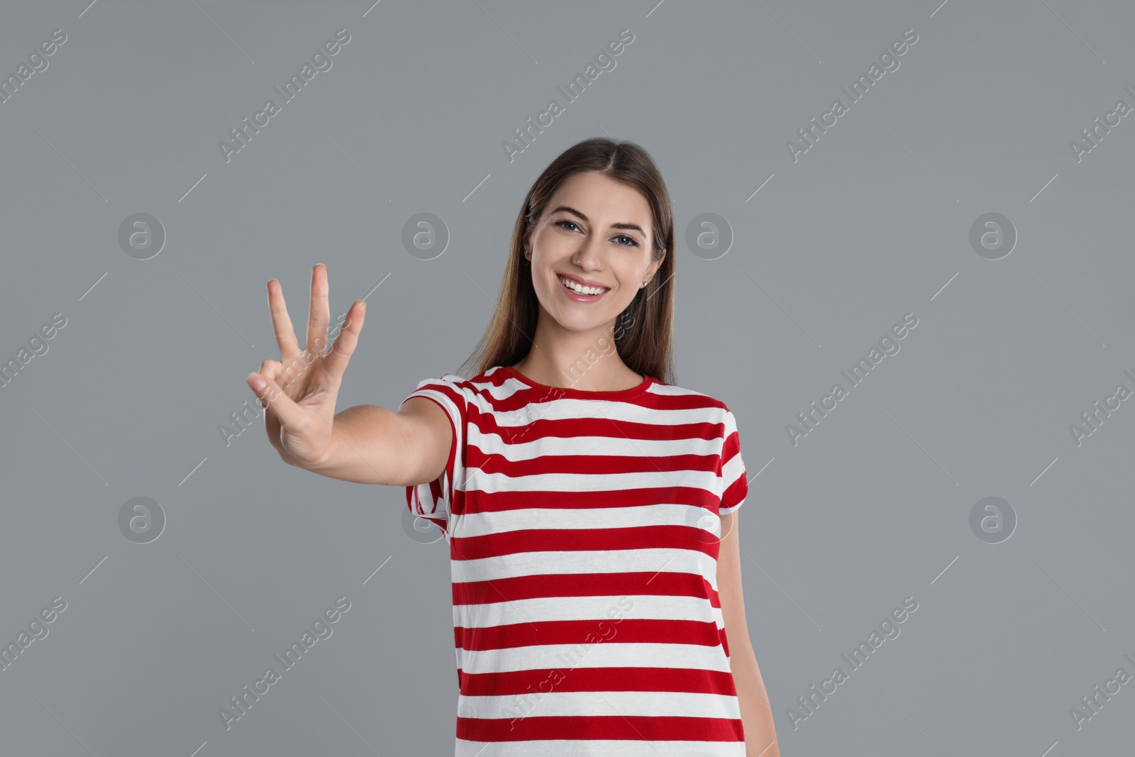 Photo of Woman showing number three with her hand on grey background