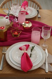 Color accent table setting. Glasses, plates, pink napkins and burning candles, closeup