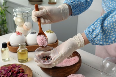 Photo of Woman in gloves making bath bomb at white table indoors, closeup