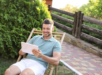 Happy man using tablet in deck chair outdoors