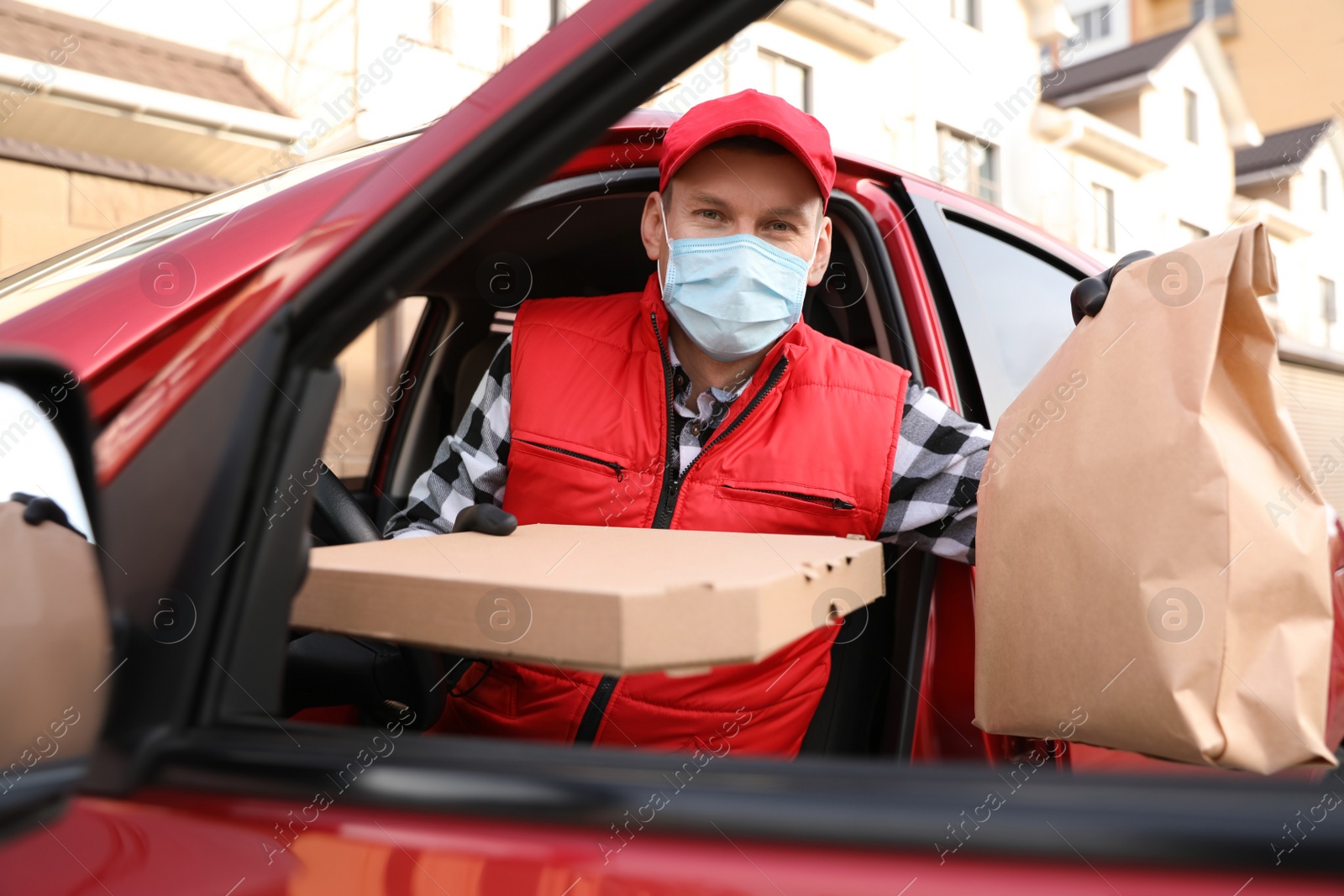 Photo of Courier in protective mask and gloves with orders getting out of car outdoors. Food delivery service during coronavirus quarantine