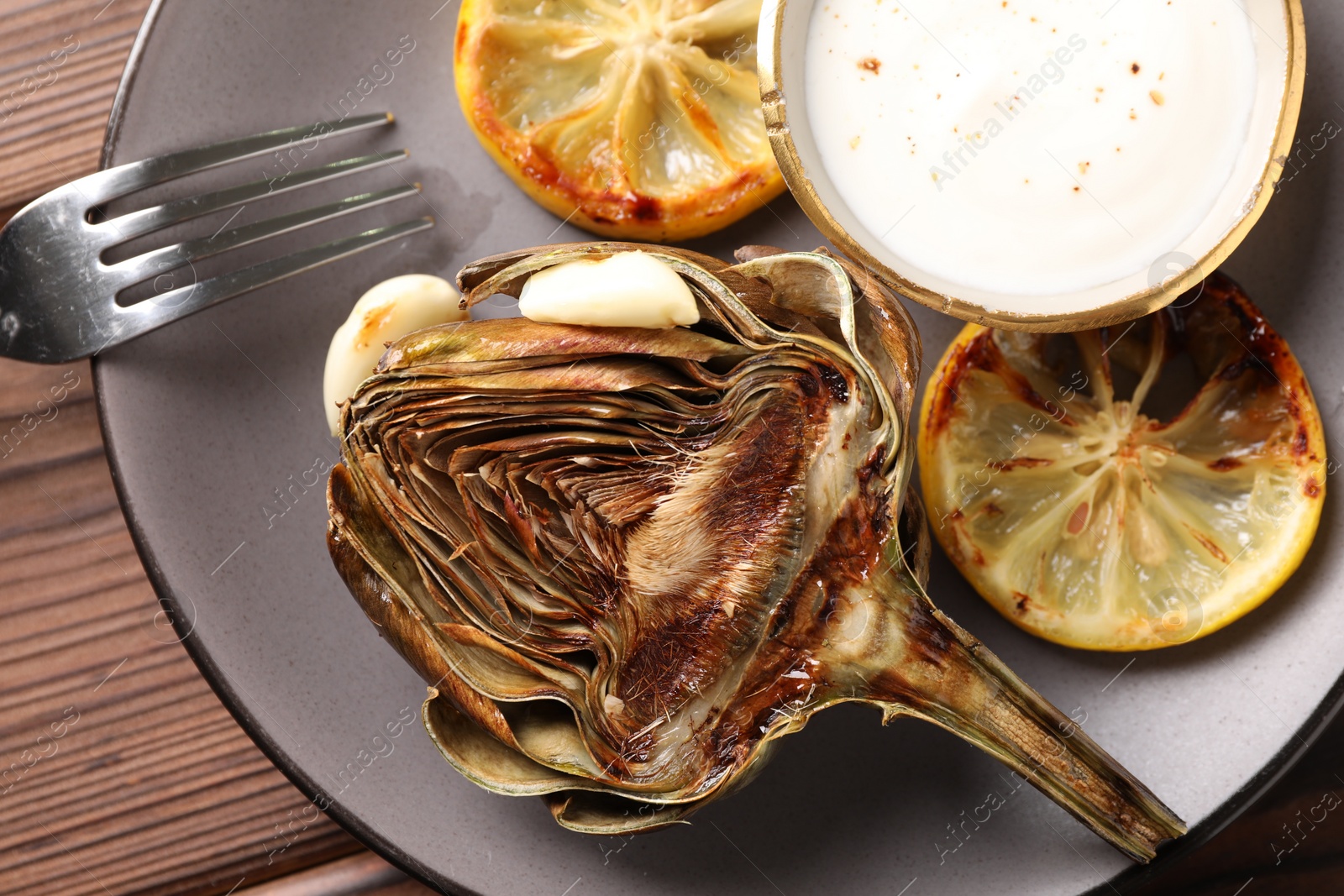 Photo of Tasty grilled artichoke served on wooden table, flat lay