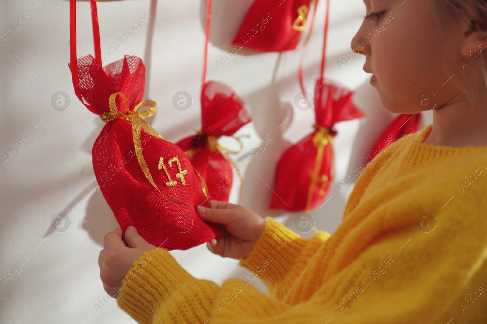 Photo of Little girl taking gift from Christmas advent calendar indoors, closeup