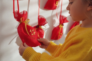 Photo of Little girl taking gift from Christmas advent calendar indoors, closeup