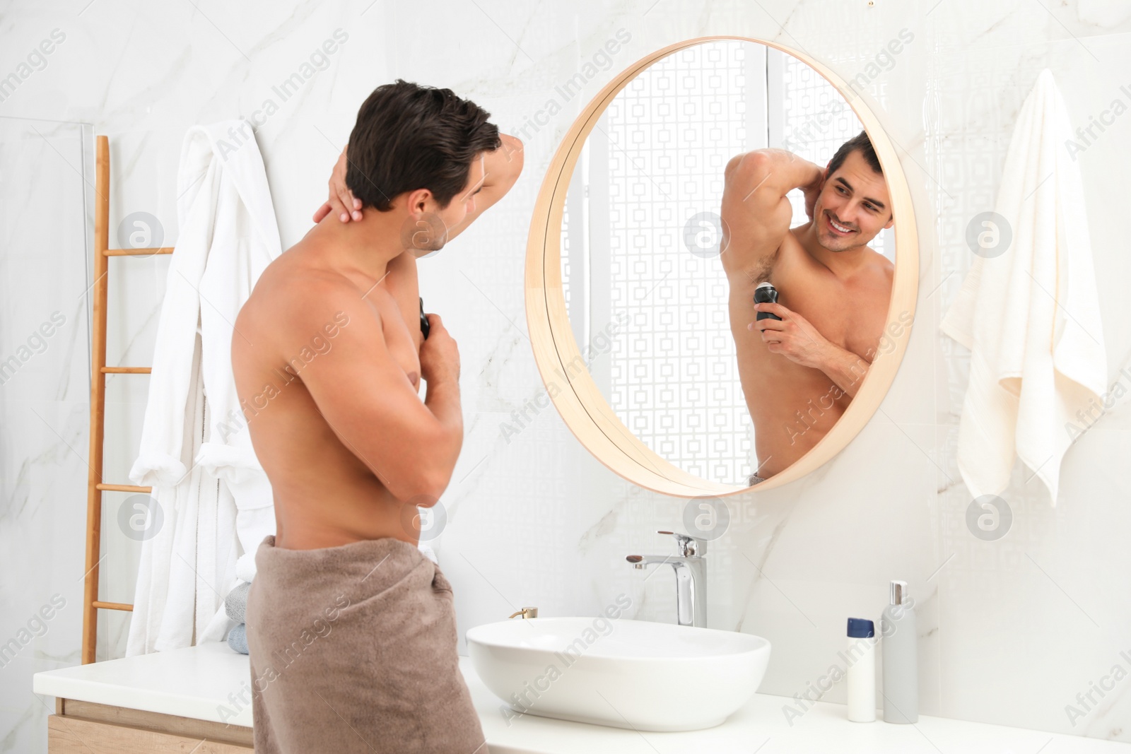 Photo of Handsome young man applying deodorant in bathroom