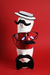Photo of Men's faces made of cups, fake mustaches, glasses, hat and bow tie on red background