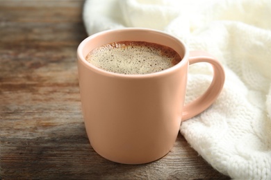 Photo of Cup of hot winter drink and knitted plaid on wooden background. Cozy season