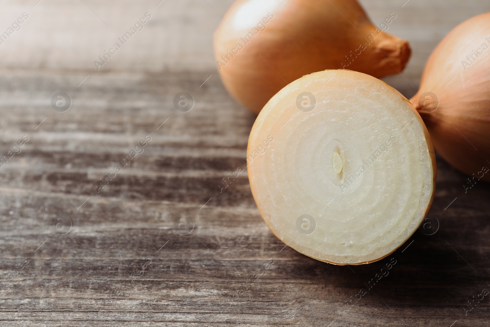 Photo of Whole and cut onions on wooden table, closeup. Space for text