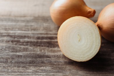 Photo of Whole and cut onions on wooden table, closeup. Space for text