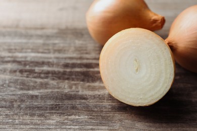 Whole and cut onions on wooden table, closeup. Space for text