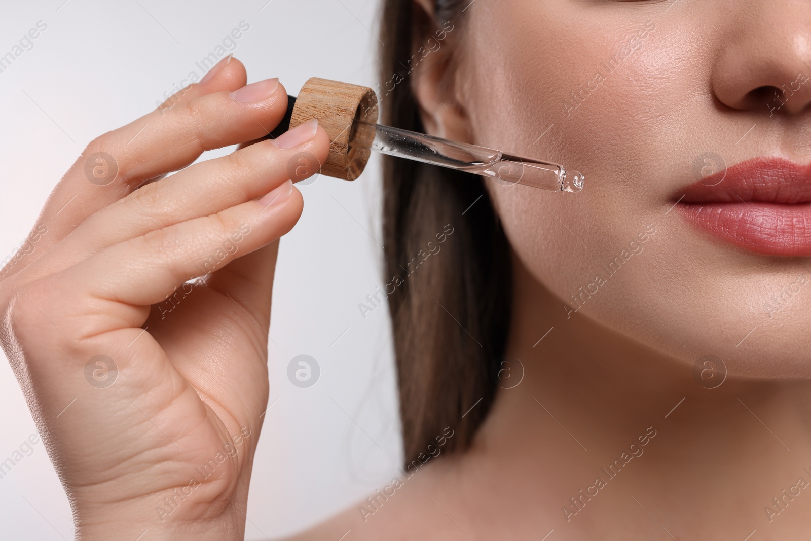 Photo of Woman applying essential oil onto face on white background, closeup