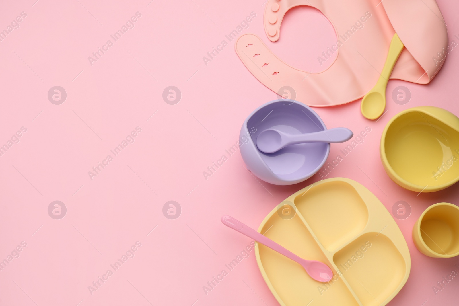 Photo of Flat lay composition with baby feeding accessories and bib on pink background, space for text