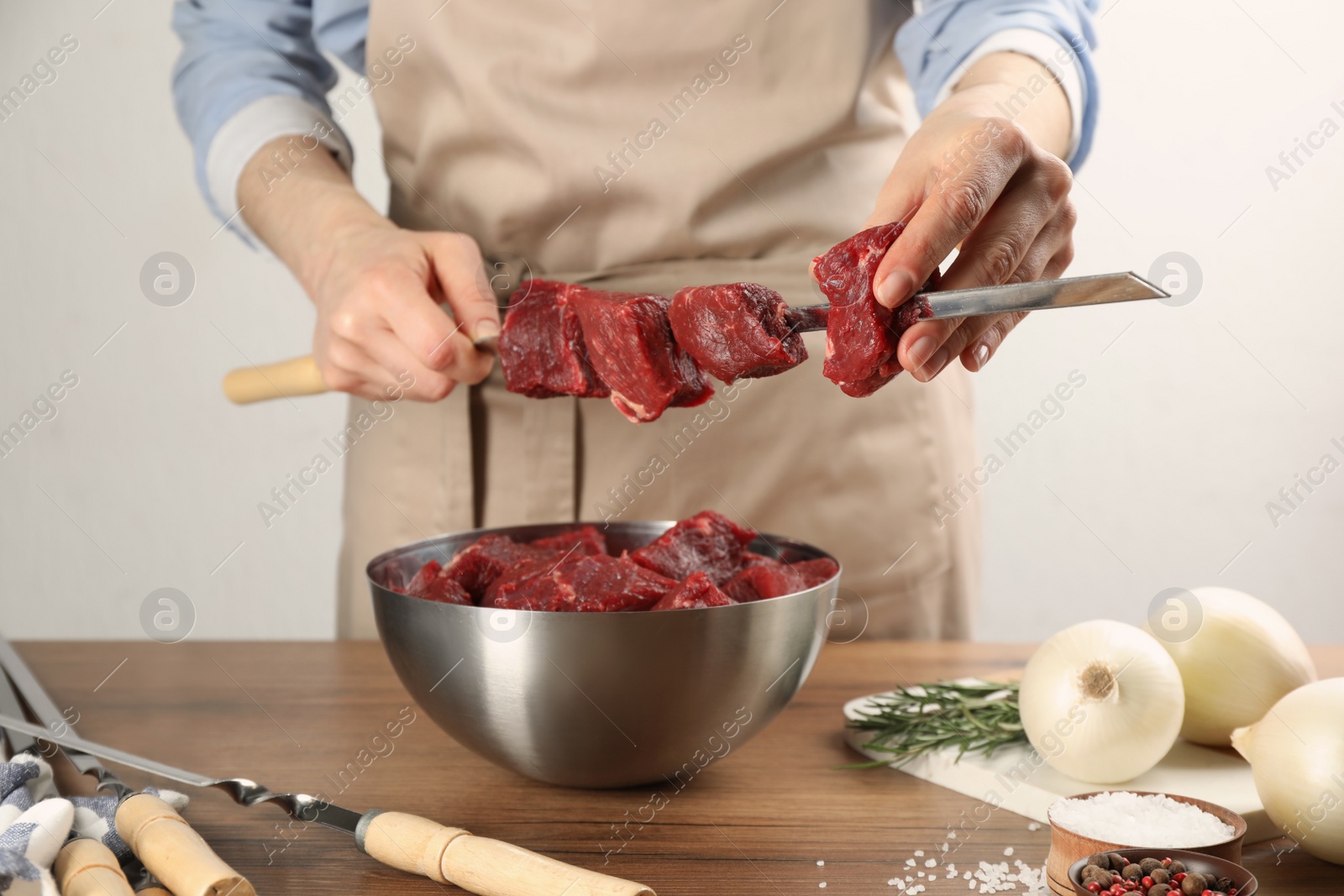 Photo of Woman stringing marinated meat on skewer at wooden table, closeup