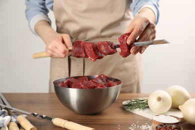 Photo of Woman stringing marinated meat on skewer at wooden table, closeup