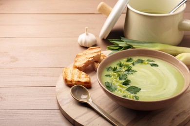 Photo of Delicious leek soup served on beige wooden table. Space for text