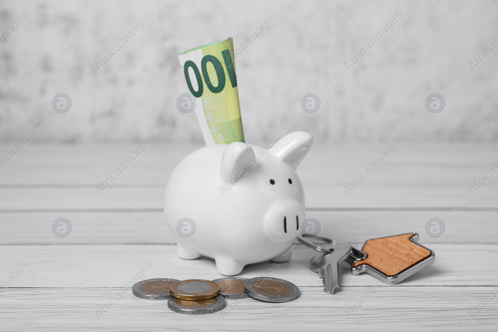 Photo of Ceramic piggy bank, coins, euro banknote and key on white wooden table. Financial savings