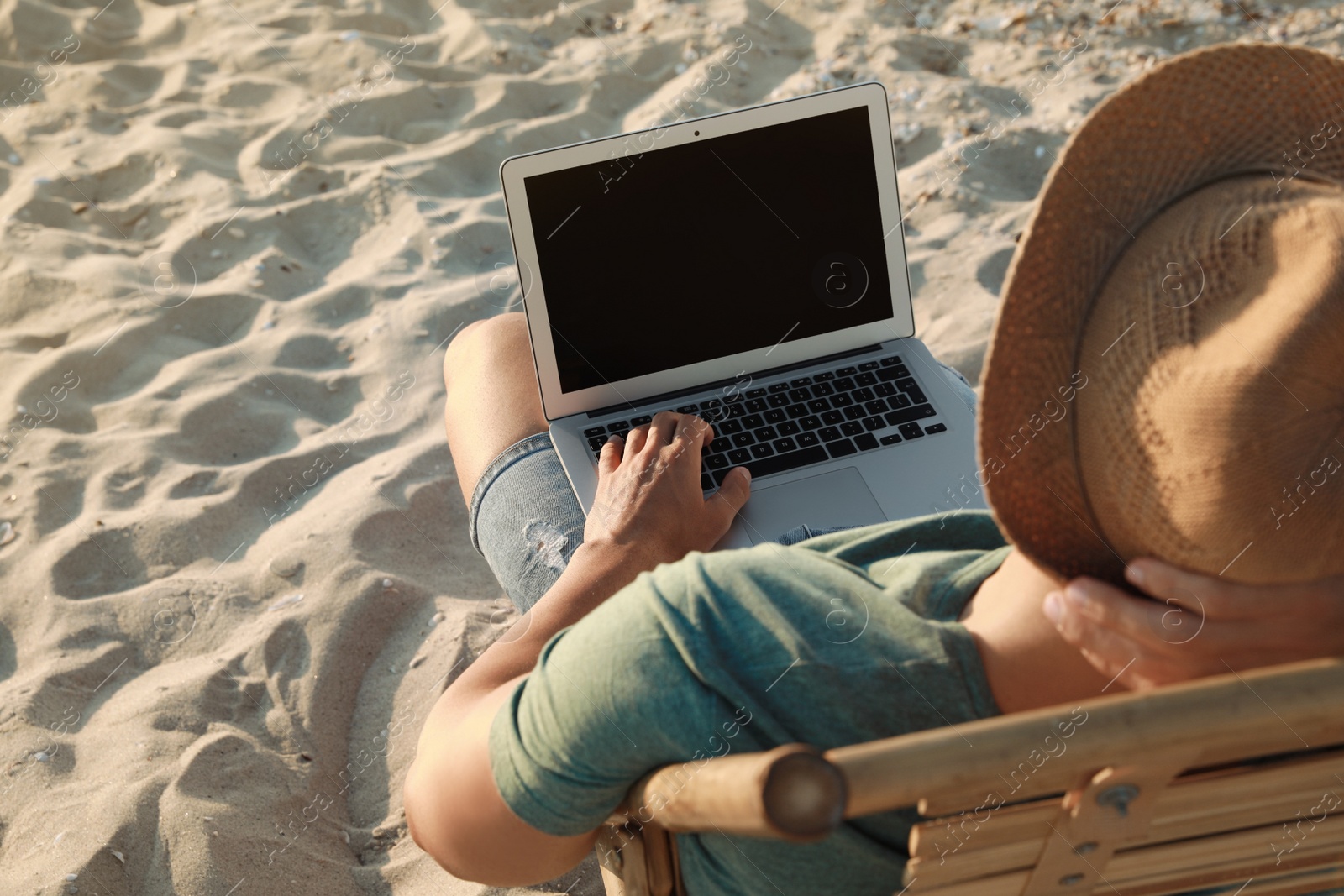 Photo of Man working with laptop in deck chair on beach, closeup