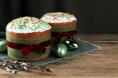 Photo of Traditional Easter cakes, painted eggs and willows on wooden table. Space for text