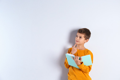 Photo of Cute little boy with book on light background, space for text