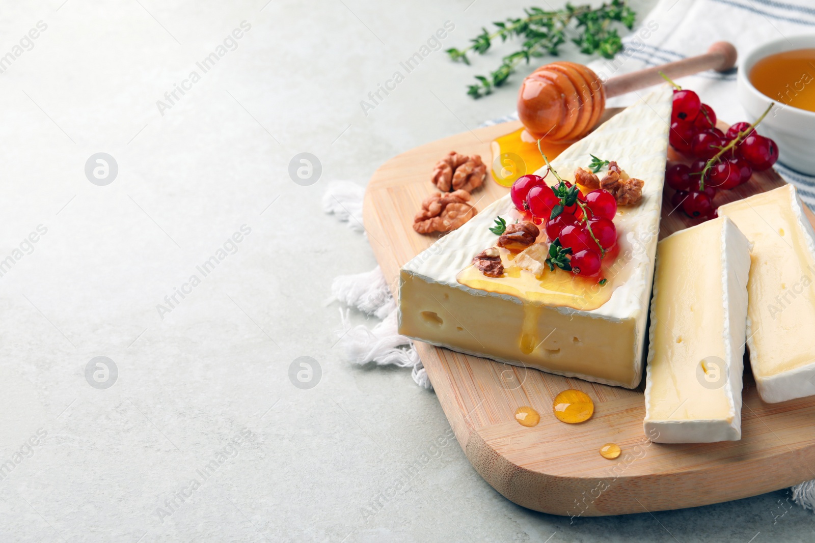 Photo of Brie cheese served with red currants, walnuts and honey on light table. Space for text