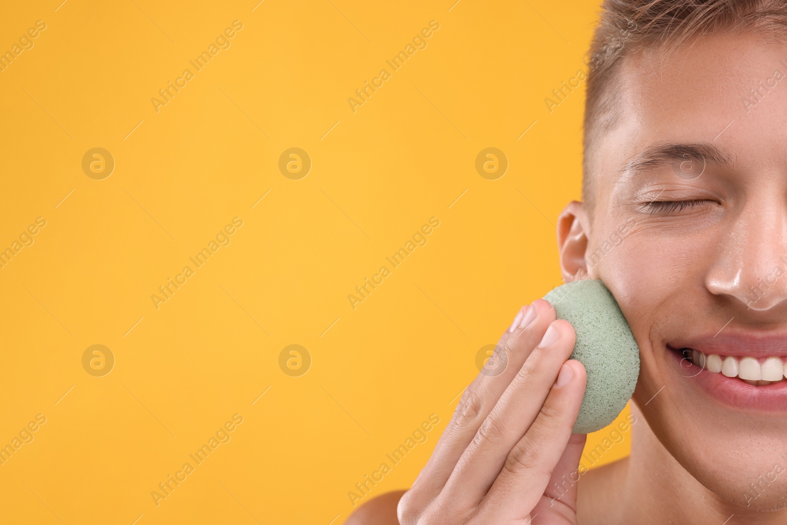 Photo of Happy young man washing his face with sponge on orange background, closeup. Space for text