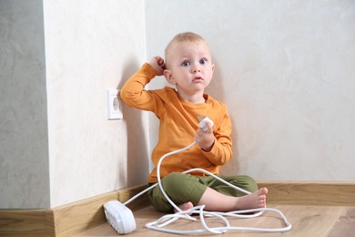Photo of Little child playing with power strip plug near electrical socket at home. Dangerous situation